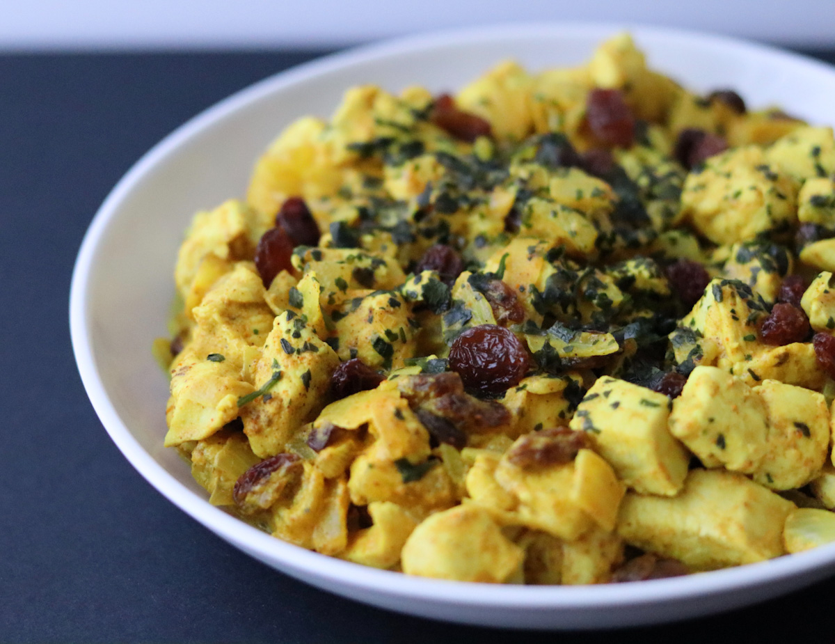 chicken curry with coconut milk with raisins  and chopped cilantro on top on a white plate 