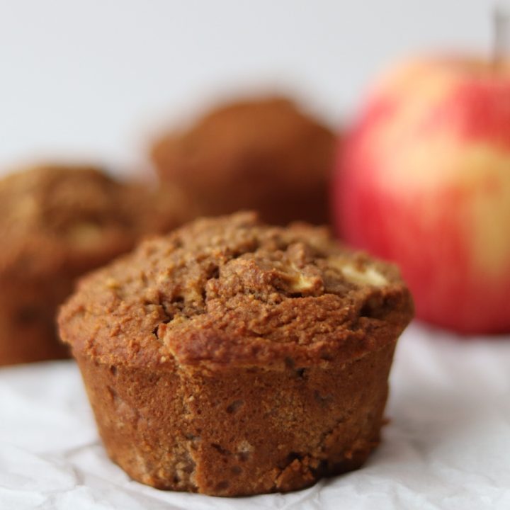 3 apple cinnamon muffins on a with sheet and an apple