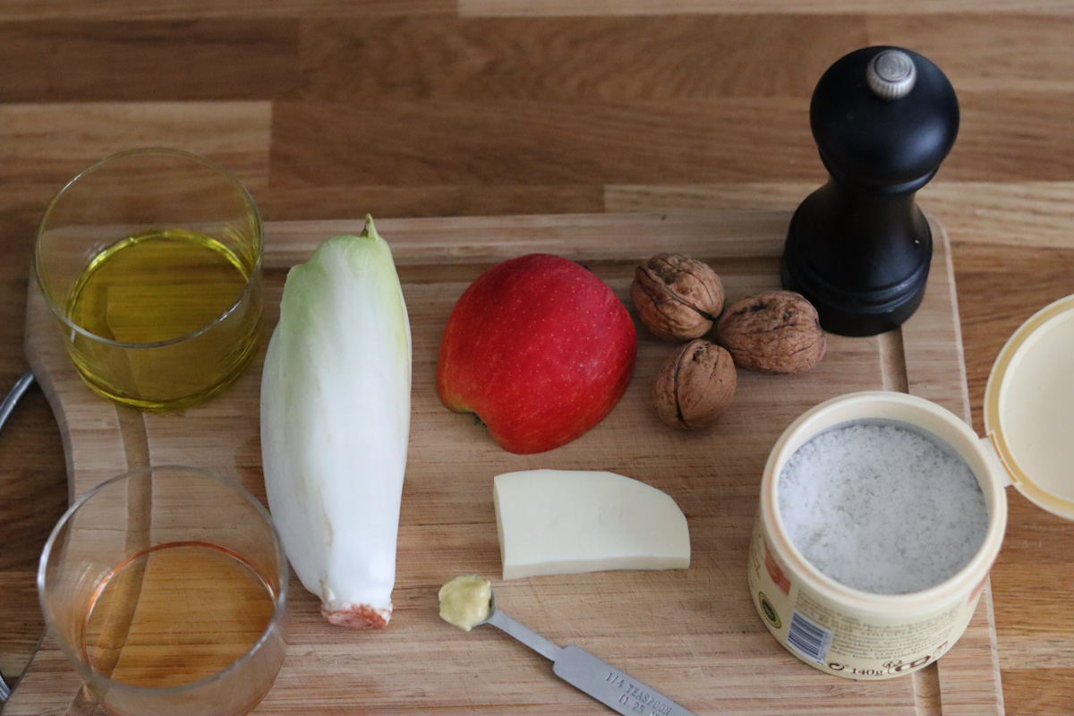 all the ingredients for the endive salad prepared on a wooden cutting board