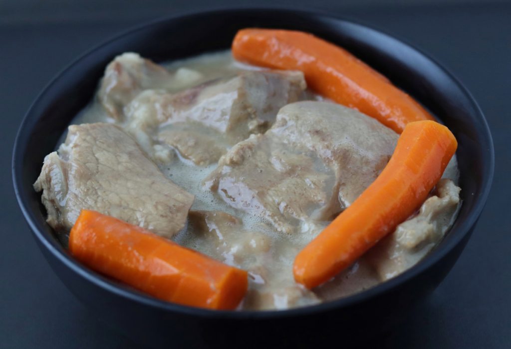 French veal stew in a black bowl with 3 carrots on top of it