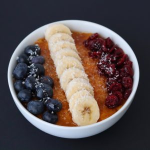 sliced banana, blueberries and dried cranberries on top of butternut squash puree in a white breakfast bowl