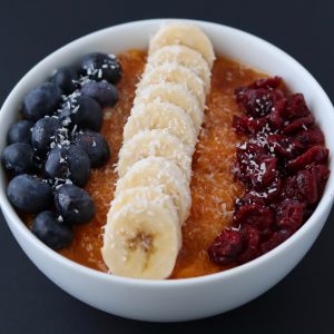 sliced banana, blueberries and dried cranberries on top of butternut squash puree in a white breakfast bowl