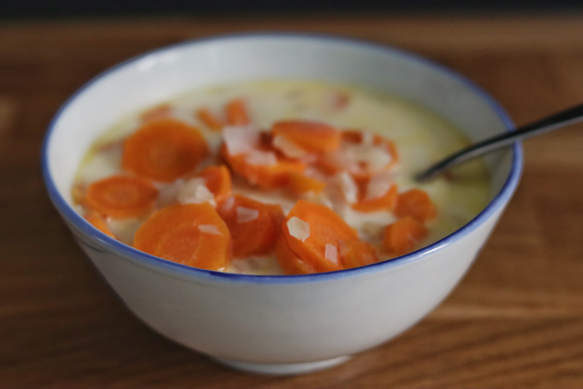 carrot coconut soup in a white and blue bowl on a kitchen counter