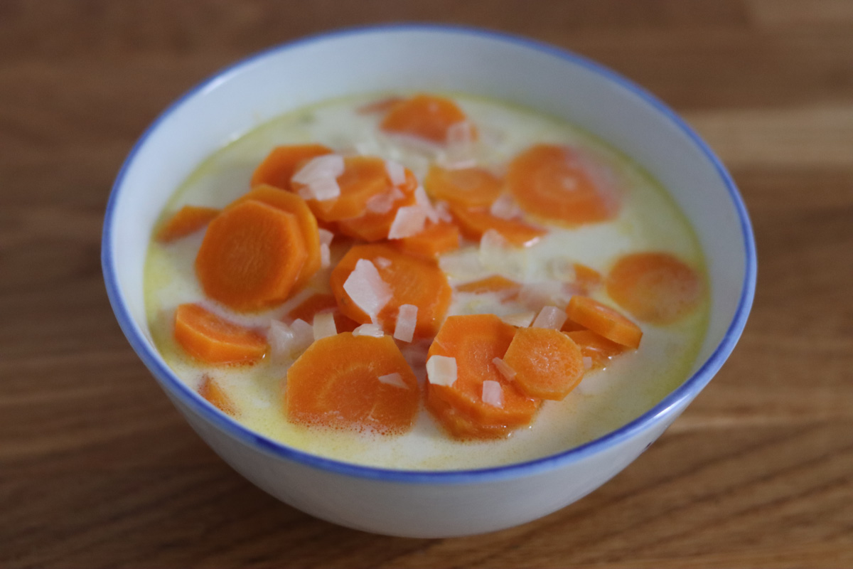 chunky carrot soup in a white bowl on a wooden kitchen counter