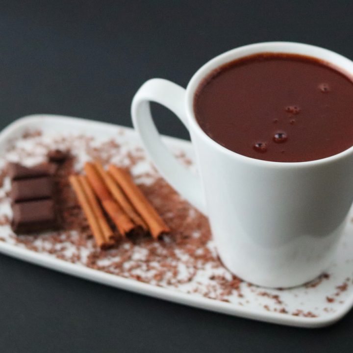a cup of hot chocolate on a white plate with cinnamon sticks and a chocolate bar