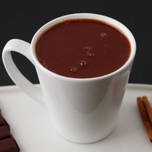 a cup of hot chocolate on a white plate with cinnamon sticks and a chocolate bar
