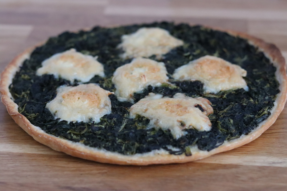 a spinach and goat cheese tart on a wooden kitchen table