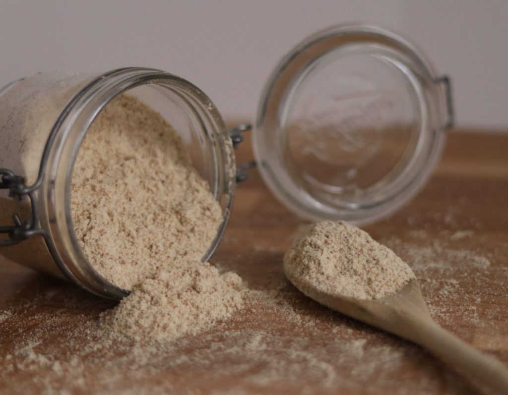 A jar of tigernut flour spilled on the kitchen counter and a wooden spoon filled with tigernut flour