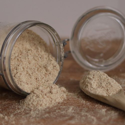 A jar of tigernut flour spilled on the kitchen counter and a wooden spoon filled with tigernut flour