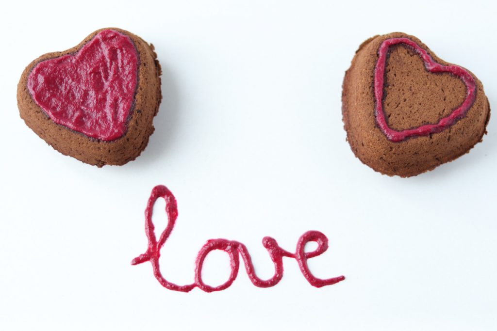 2 heart shaped chocolate cakes with no dye pink frosting on top and the word love written with the frosting on the plate.