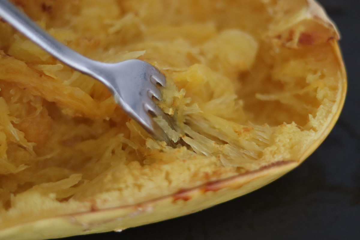 a fork scraping the flesh of a spaghetti squash to reveal the spaghetti texture