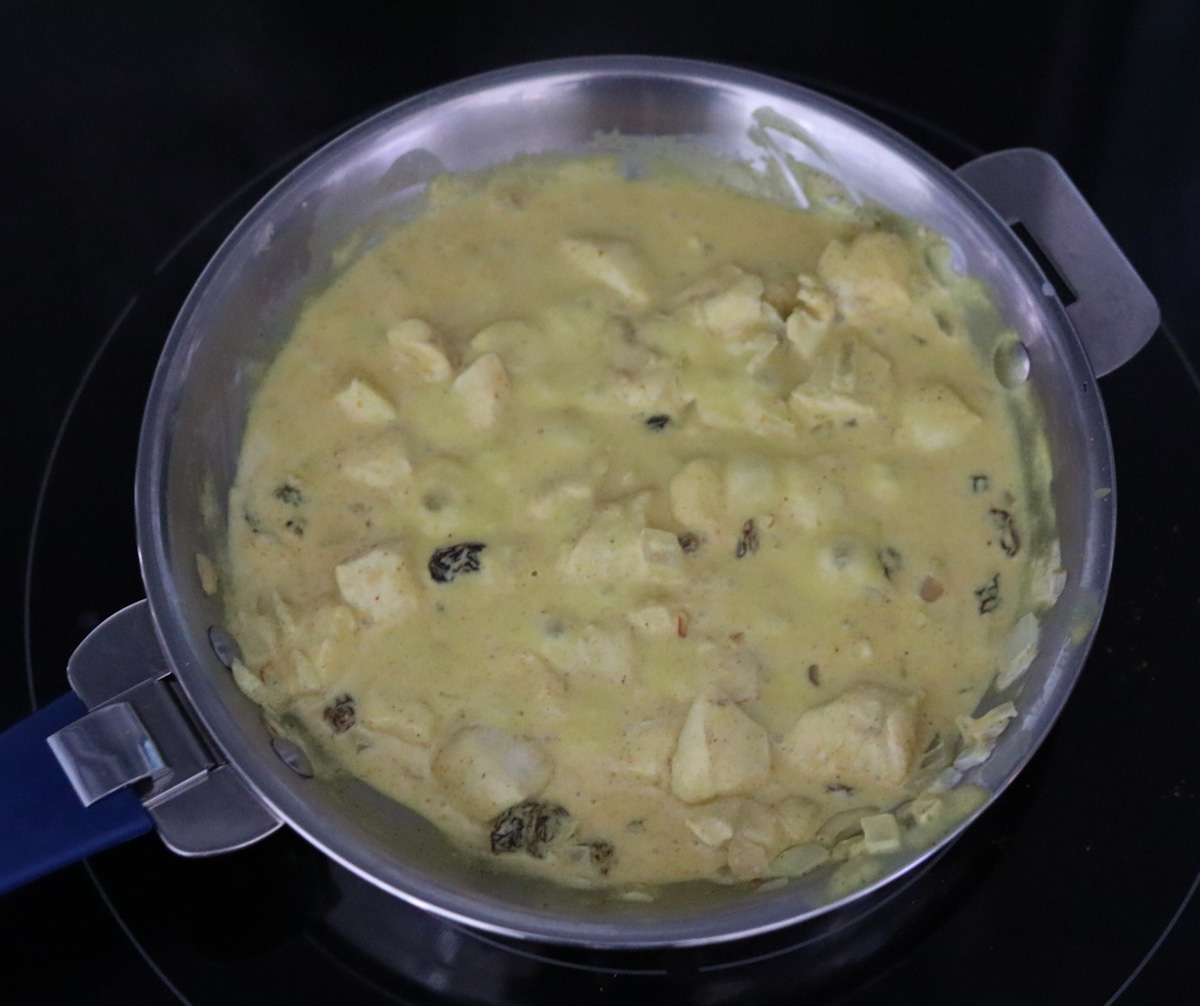 chicken, onion, raisins simmering in a rich coconut sauce in a skillet