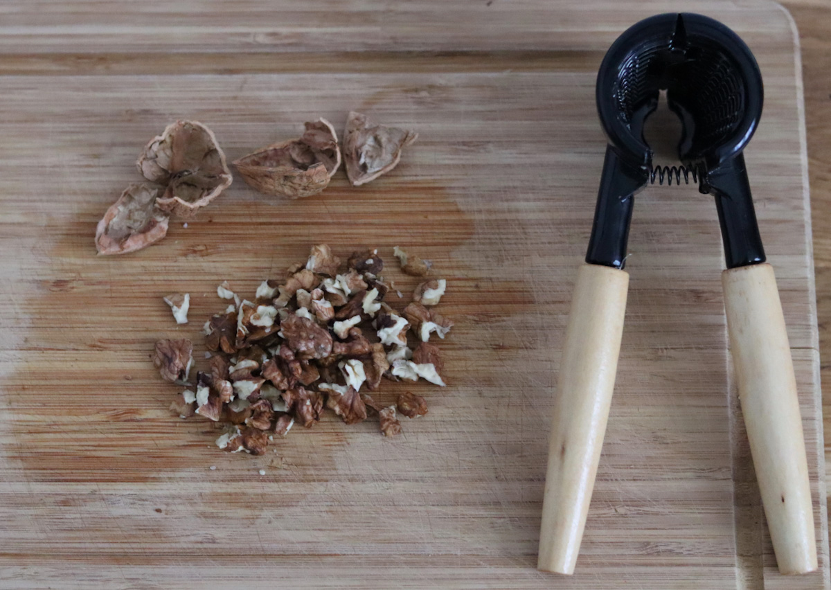 a cracked walnut with a nut cracker on a cutting board