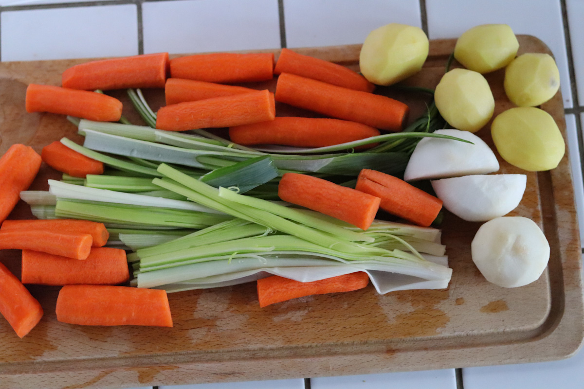 peeled and roughly cut carrots, leeks turnips and potatoes on a wooden board