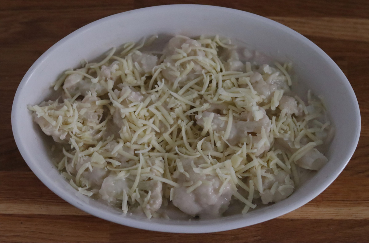 cauliflower florets topped with bechamel sauce and grated cheese in a baking dish