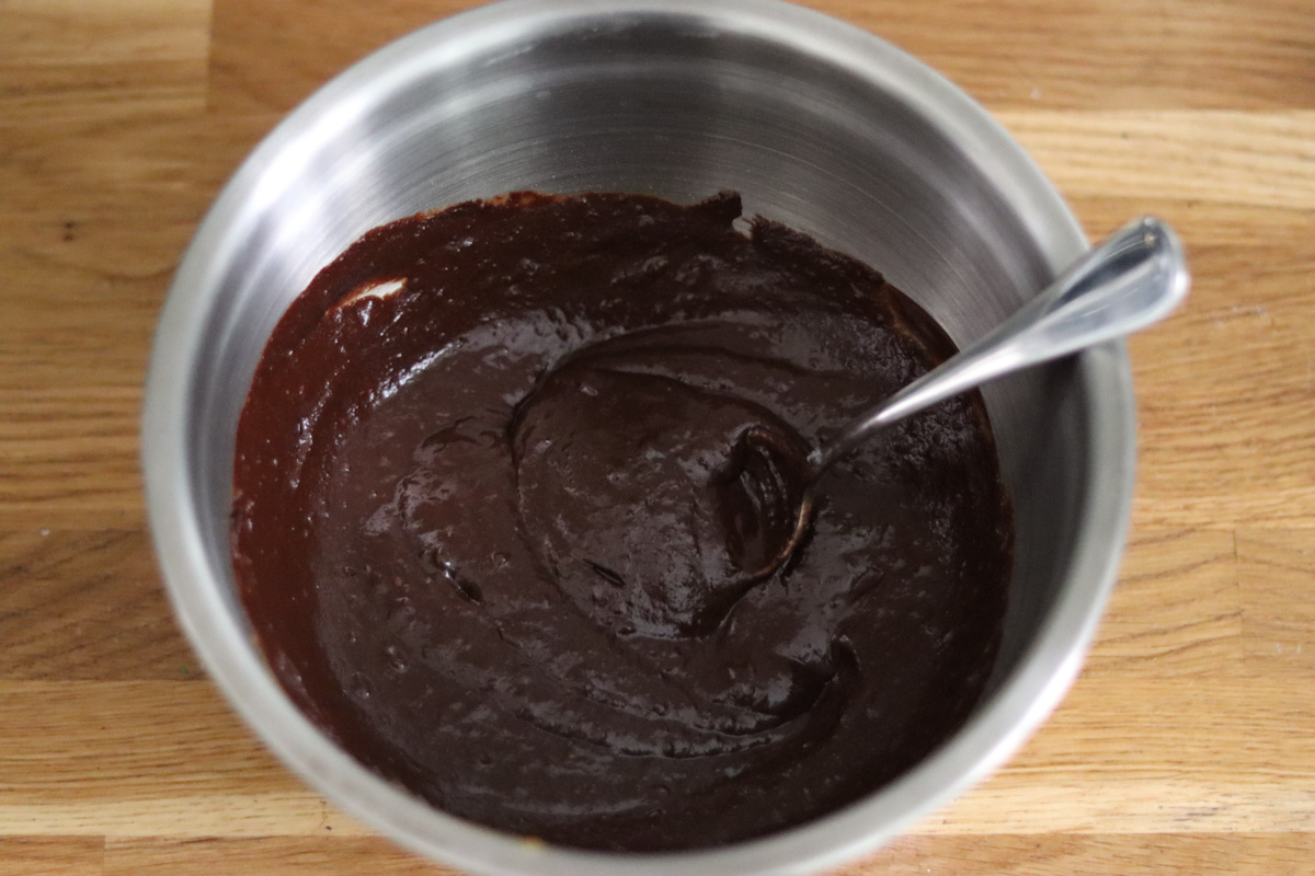 all the wet and dry ingredients for the fudgy chocolate cake combined together in a large bowl with a spoon