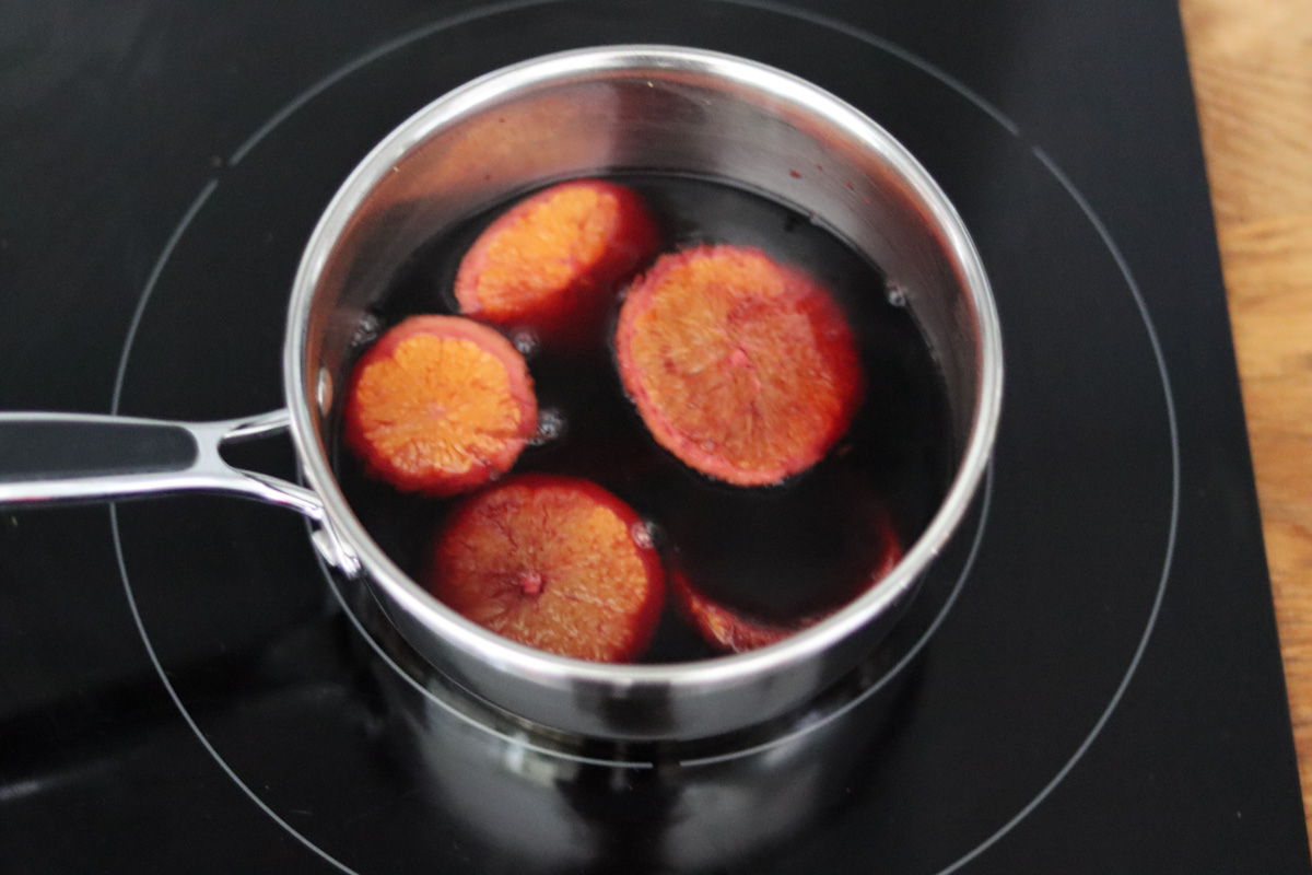 slices of orange cooking in red wine in a sauce pan on a stove top 