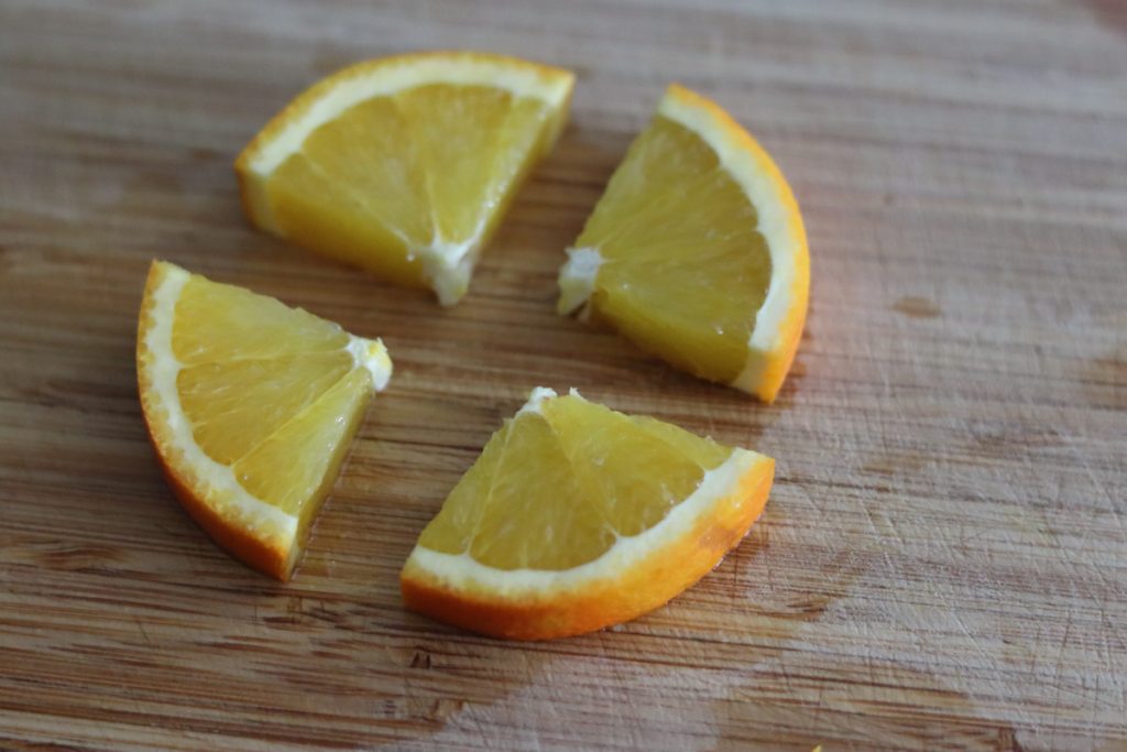 an orange slice cut in quarter on a wooden board