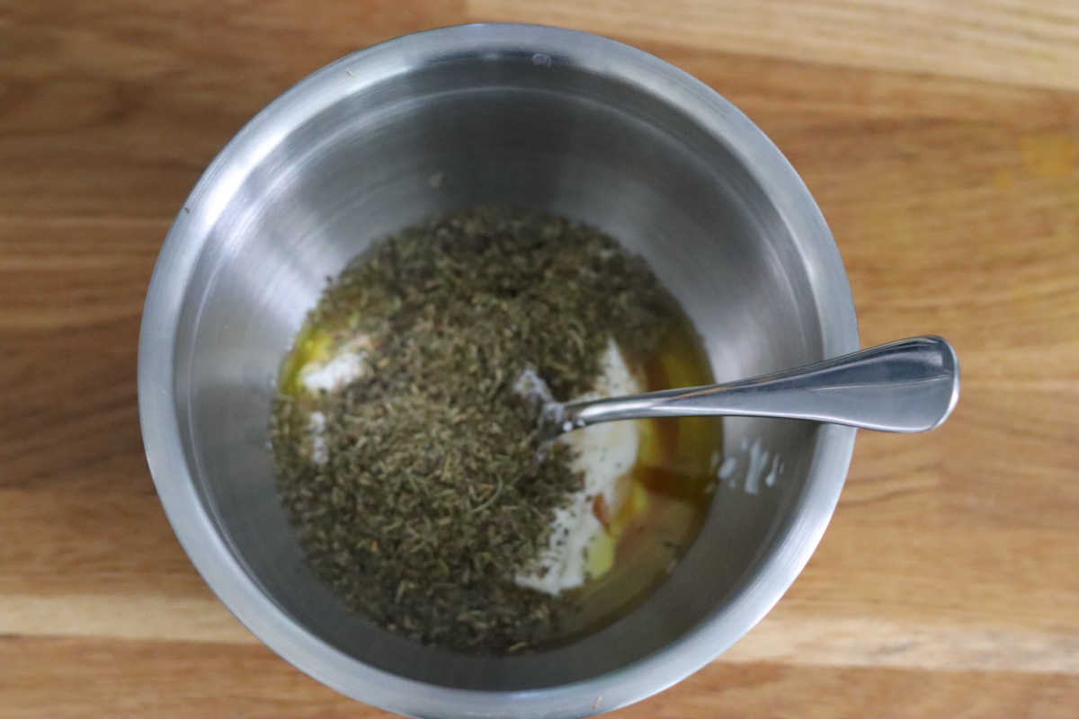 le yaourt, l’huile d’olive, le vinaigre de cidre et les herbes de Provence dans un saladier avec une cuillère