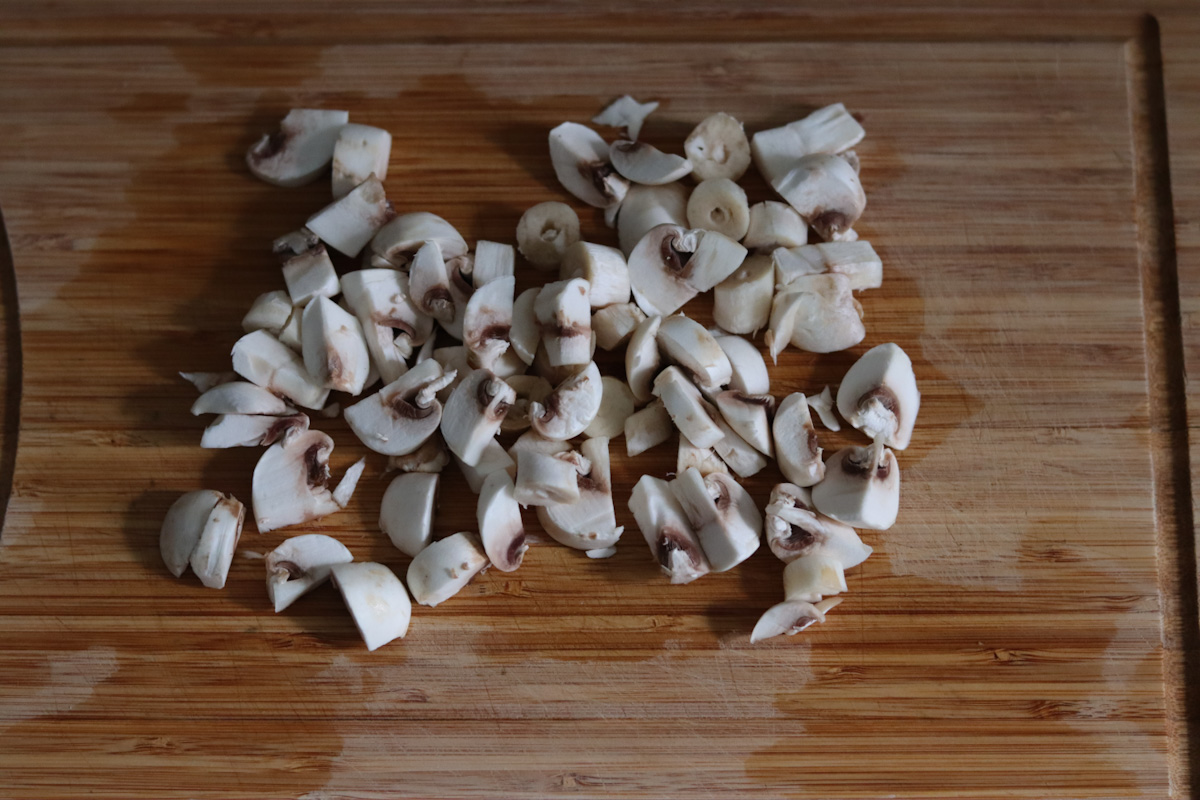 white mushrooms cut in pieces on a wooden cut board