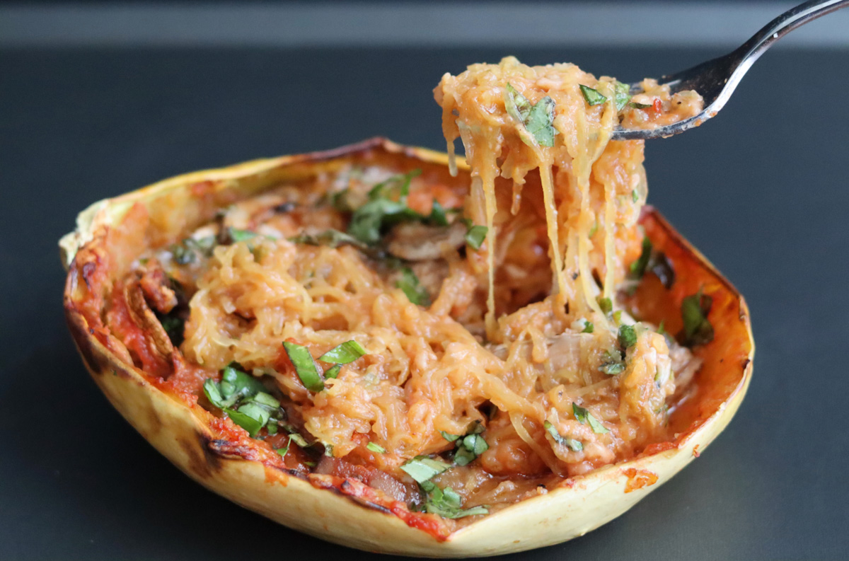 a fork taking some stuffed spaghetti squash with chopped basil on top