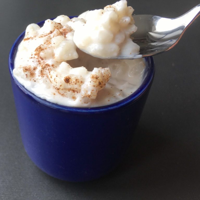 a blue cup filled with rice pudding with cinnamon sprinkled on top and a spoonful being taken out of the cup