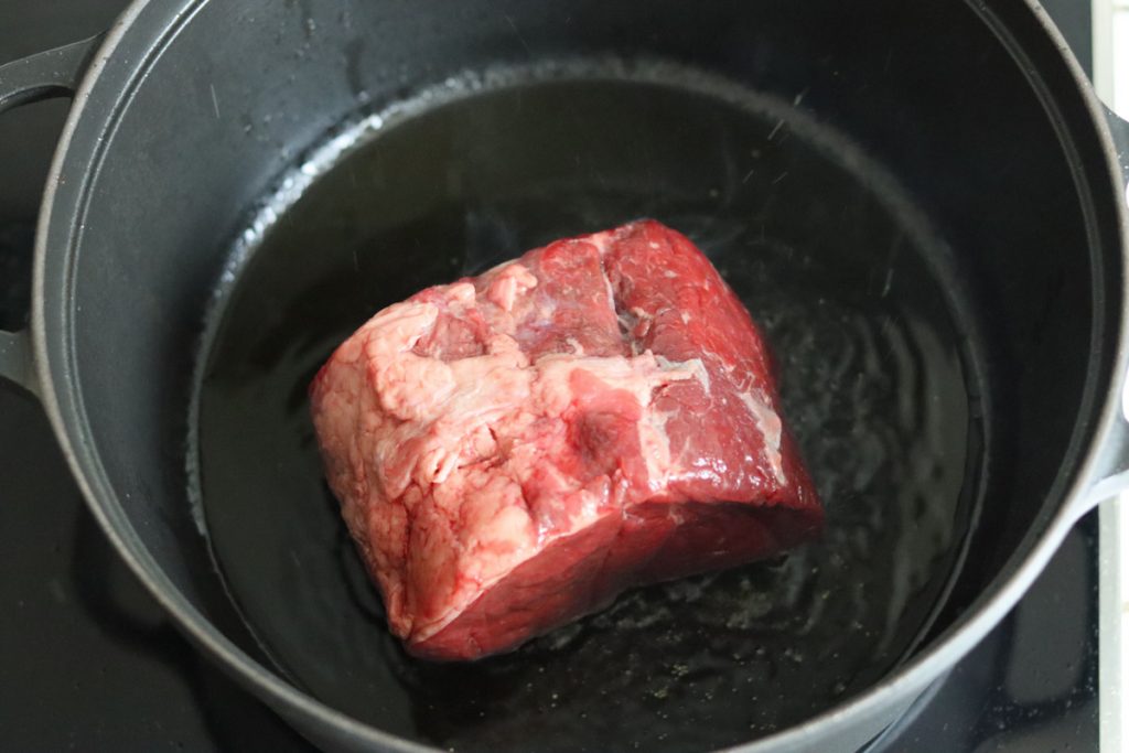 beef stew meat cooking in olive oil in a large black Dutch oven