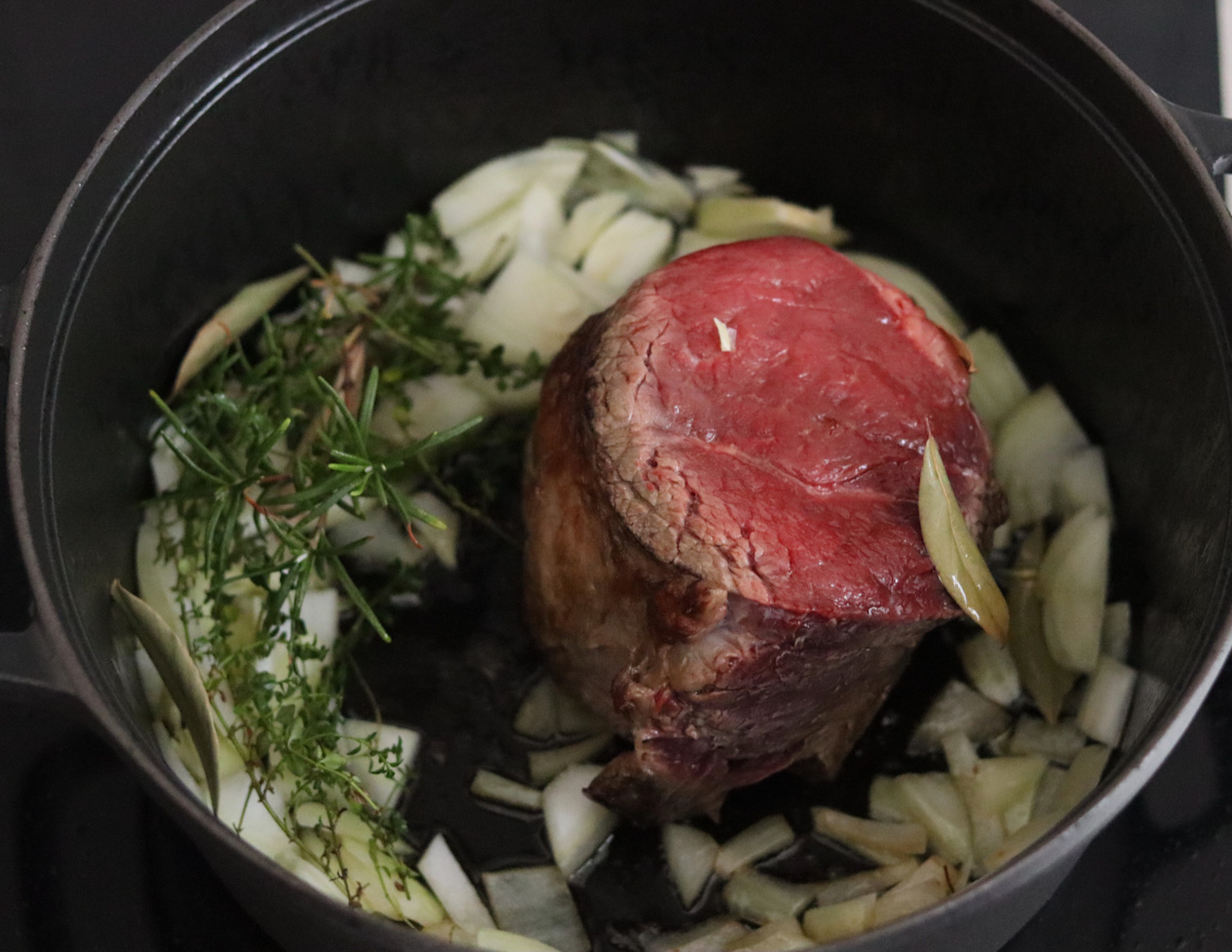 beef stew meat and diced onion and bouquet garni cooking in olive oil in a large black Dutch oven