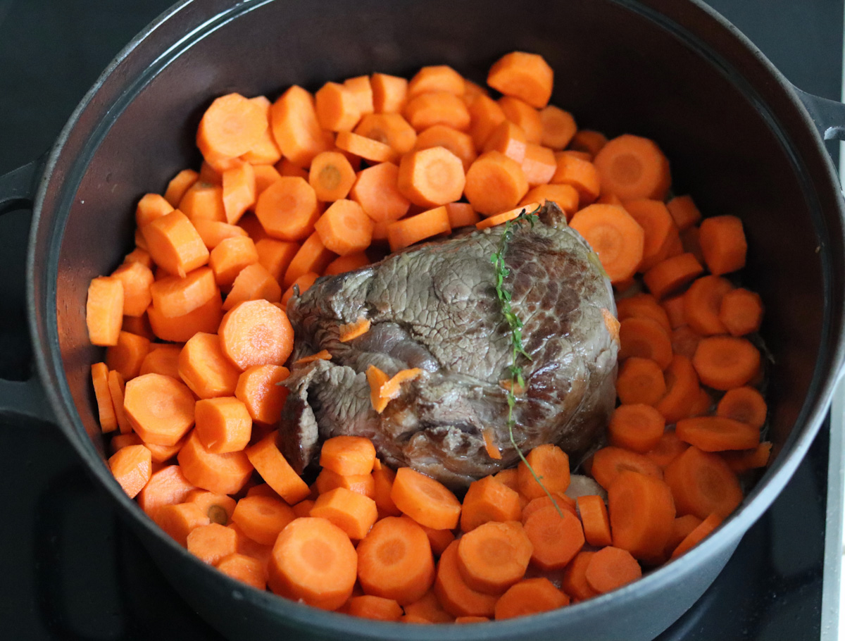 beef stew meat and sliced carrots cooking in a large black Dutch oven