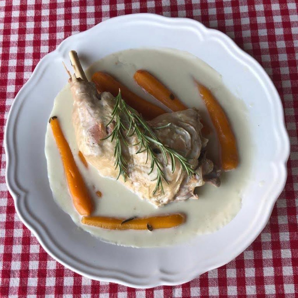 turkey leg stew with carrots and rosemary on a large white plate on a table cloth