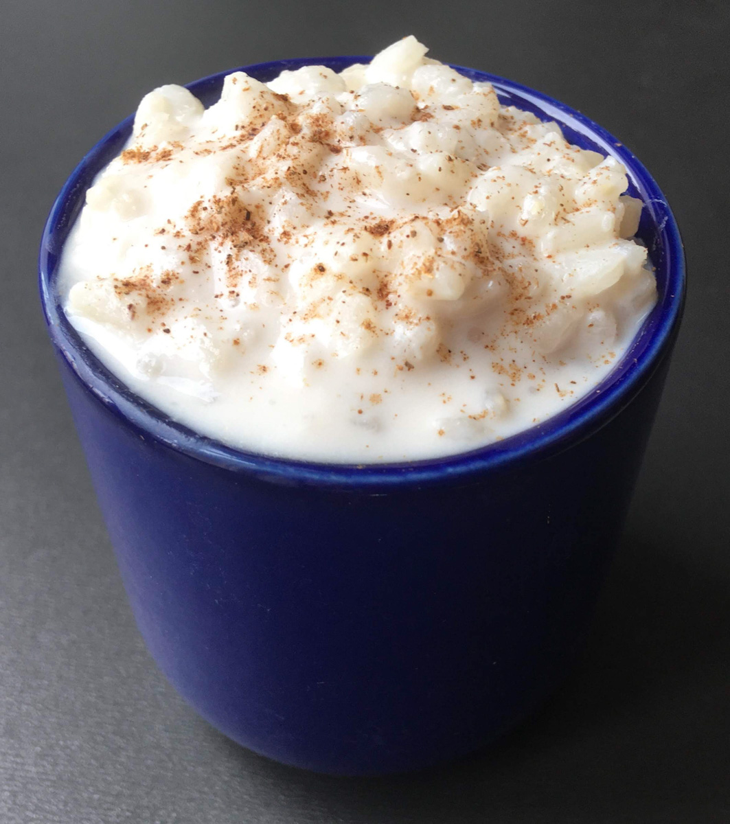 a blue cup filled with rice pudding with cinnamon sprinkled on top