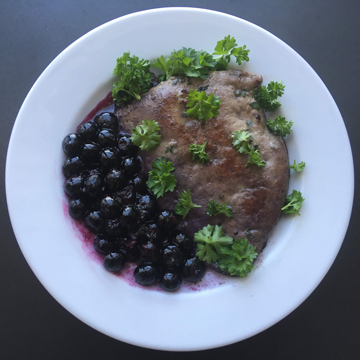 Foie veau poêlé avec du persil et des myrtilles sur une assiette blanche