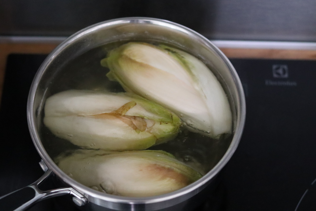 3 endives cooking in water in a sauce pan