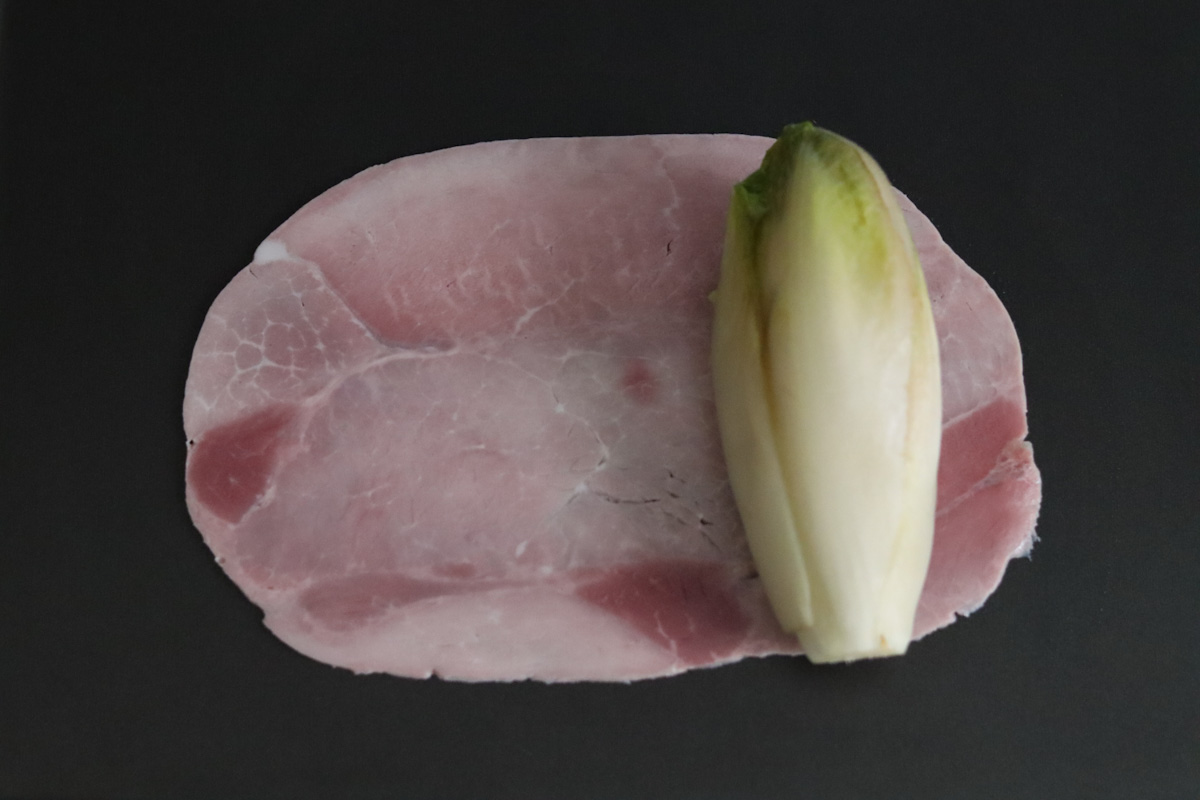an endive on top of a piece of ham, ready to be rolled