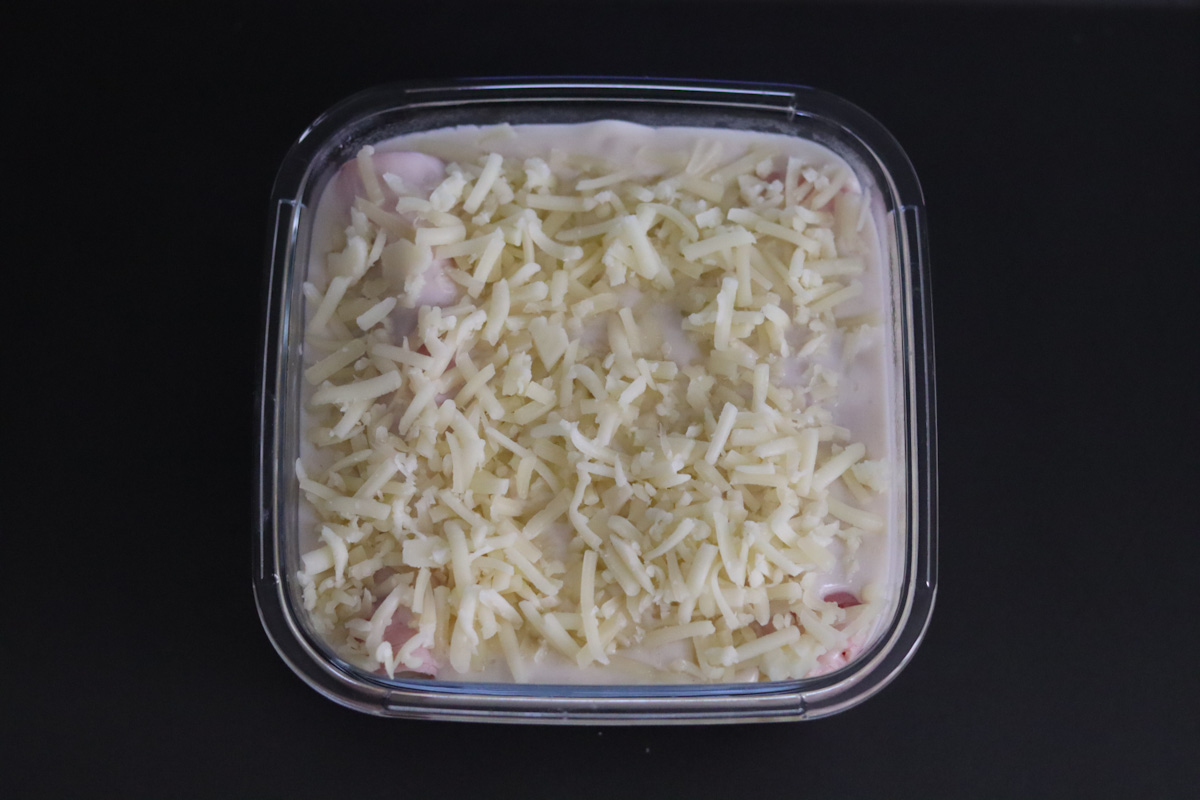 endives rolled in ham in a baking dish, topped with bechamel sauce and grated cheese