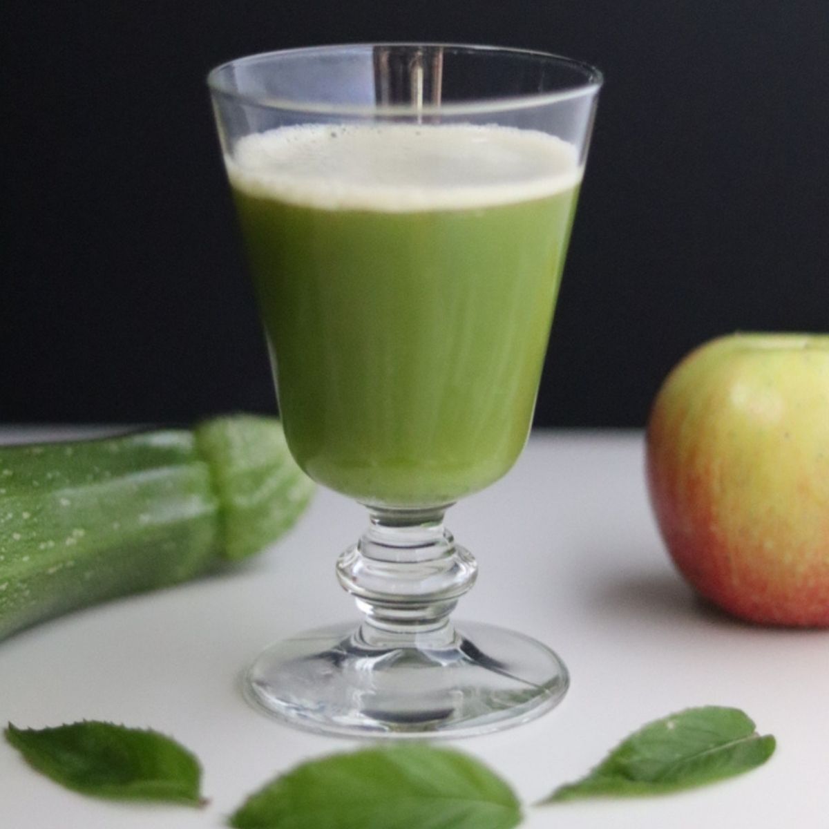 un verre de jus de pomme et courgette, une courgette, une pomme et 3 feuilles de menthe tout autour