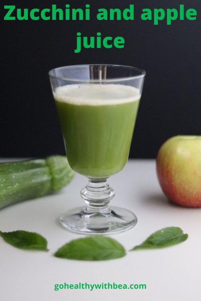 a glass of zucchini and apple juice, a zucchini, an apple and 3 mint leaves around the glass and the titla written in green letters