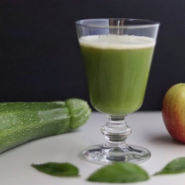 un verre de jus de pomme et courgette, une courgette, une pomme et 3 feuilles de menthe tout autour