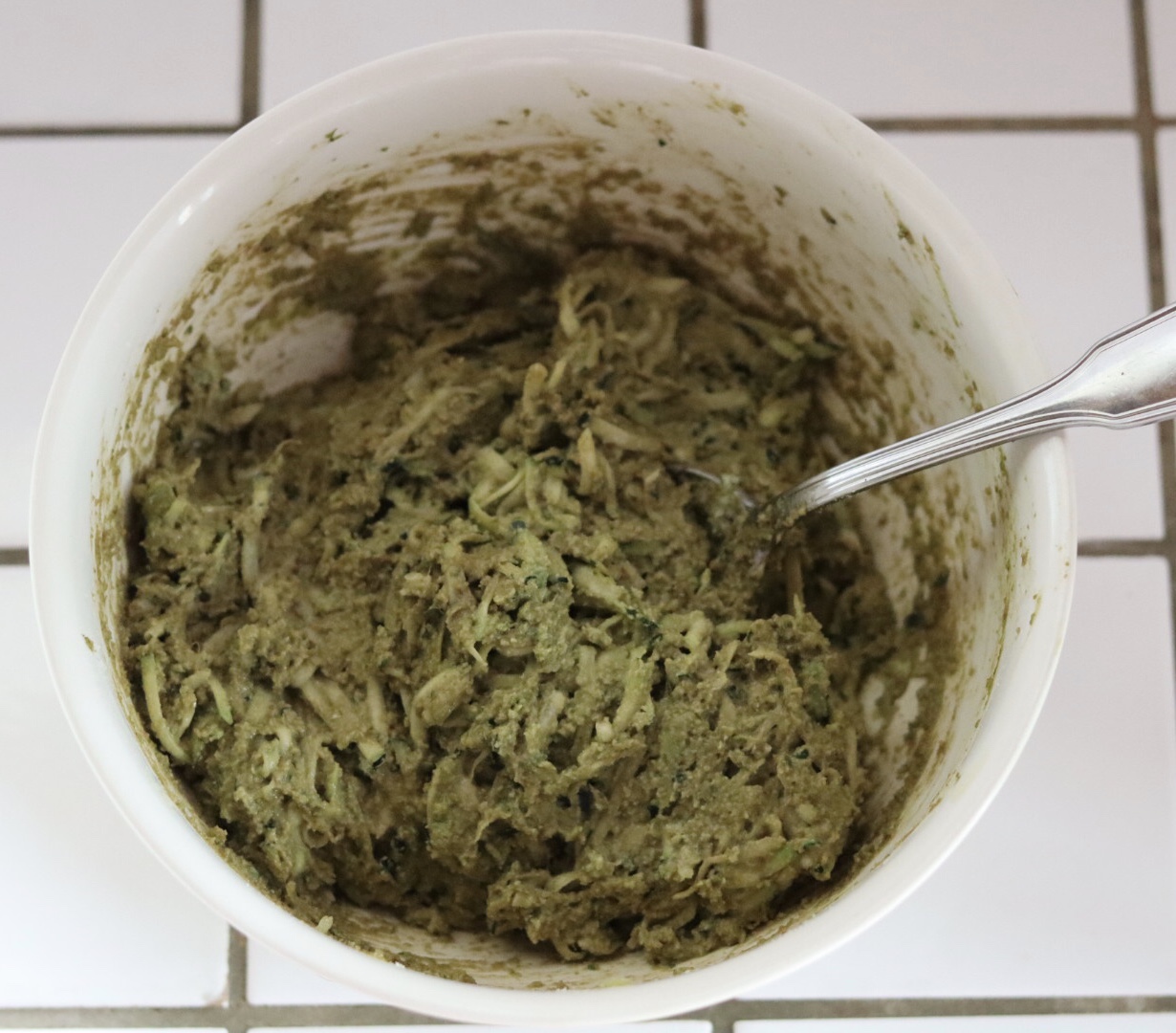 zucchini and pesto muffins batter in a white bowl on a kitchen counter