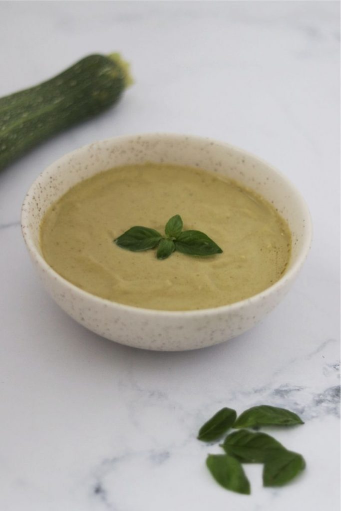a bowl of cold zucchini soup and basil leaves on top to decorate