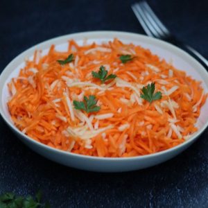 Salade de carottes râpées aux pommes dans une assiette creuse blanche et une fourchette en arrière plan