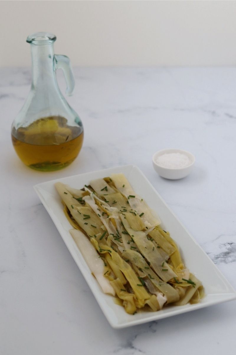 leeks salad on a white rectangular plate a bottle of olive oil and sea salt in a small bowl