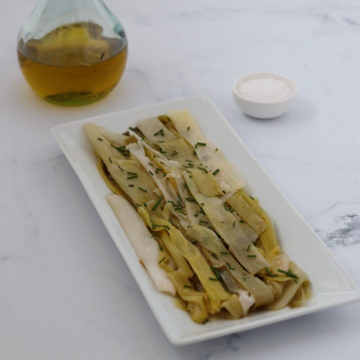 poireaux vinaigrette sur un plat rectangulaire blanc, un flacon d'huile d'olive et de la fleur de sel dans un petit bol