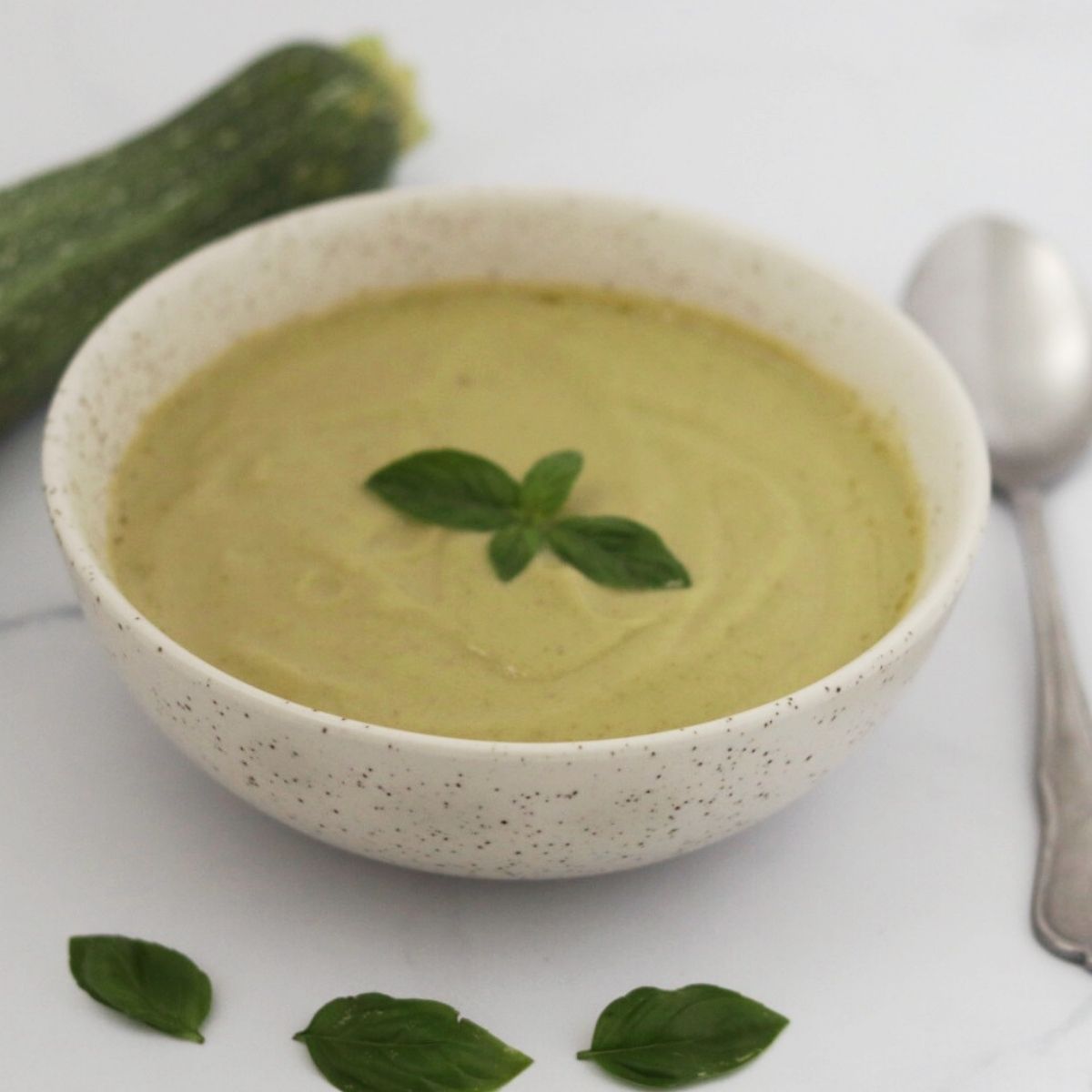 a bowl of cold zucchini soup and basil leaves on top to decorate