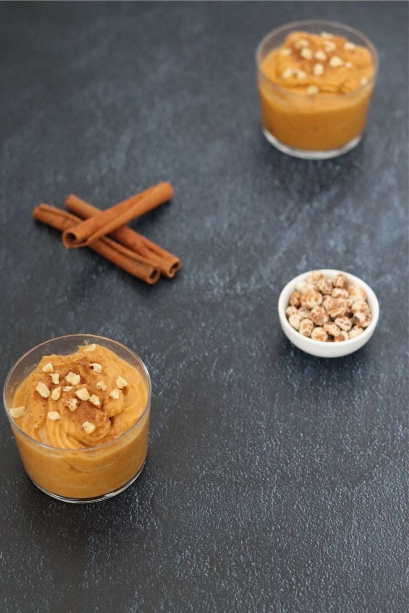 2 small cups filled with pumpkin pudding, cinnamon sticks and peeled tigernuts in a small bowl