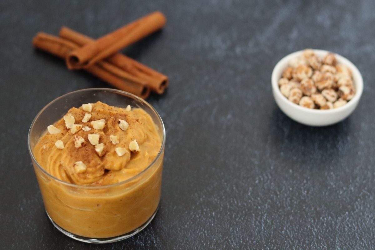 Pumpkin pudding in a small cup, cinnamon sticks in the background and peeled tigernuts in a small bowl on the side