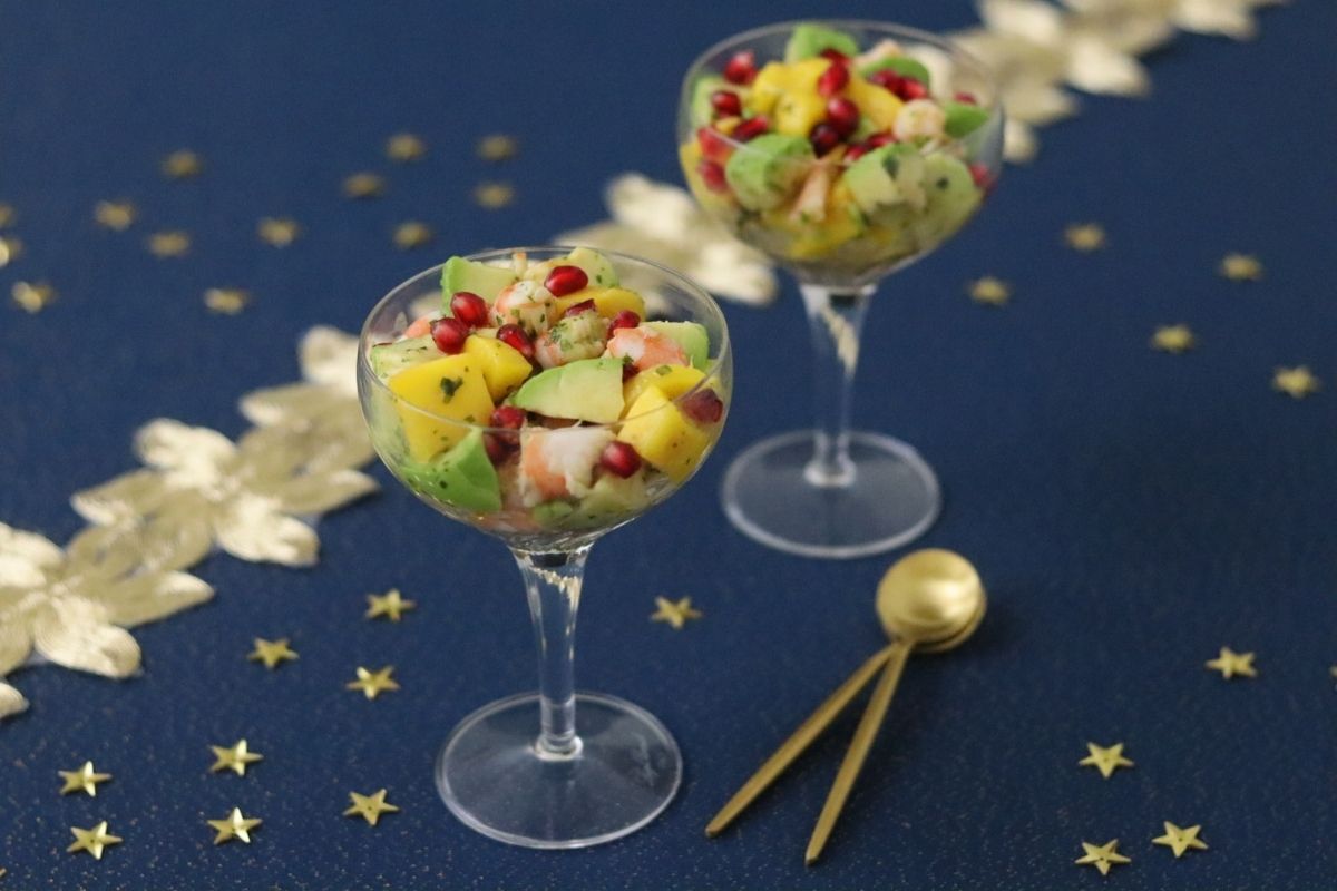 Mango avocado shrimp salad in 2 wine glasses on a night blue table cloth along with 2 golden spoons and gold stars to decorate
