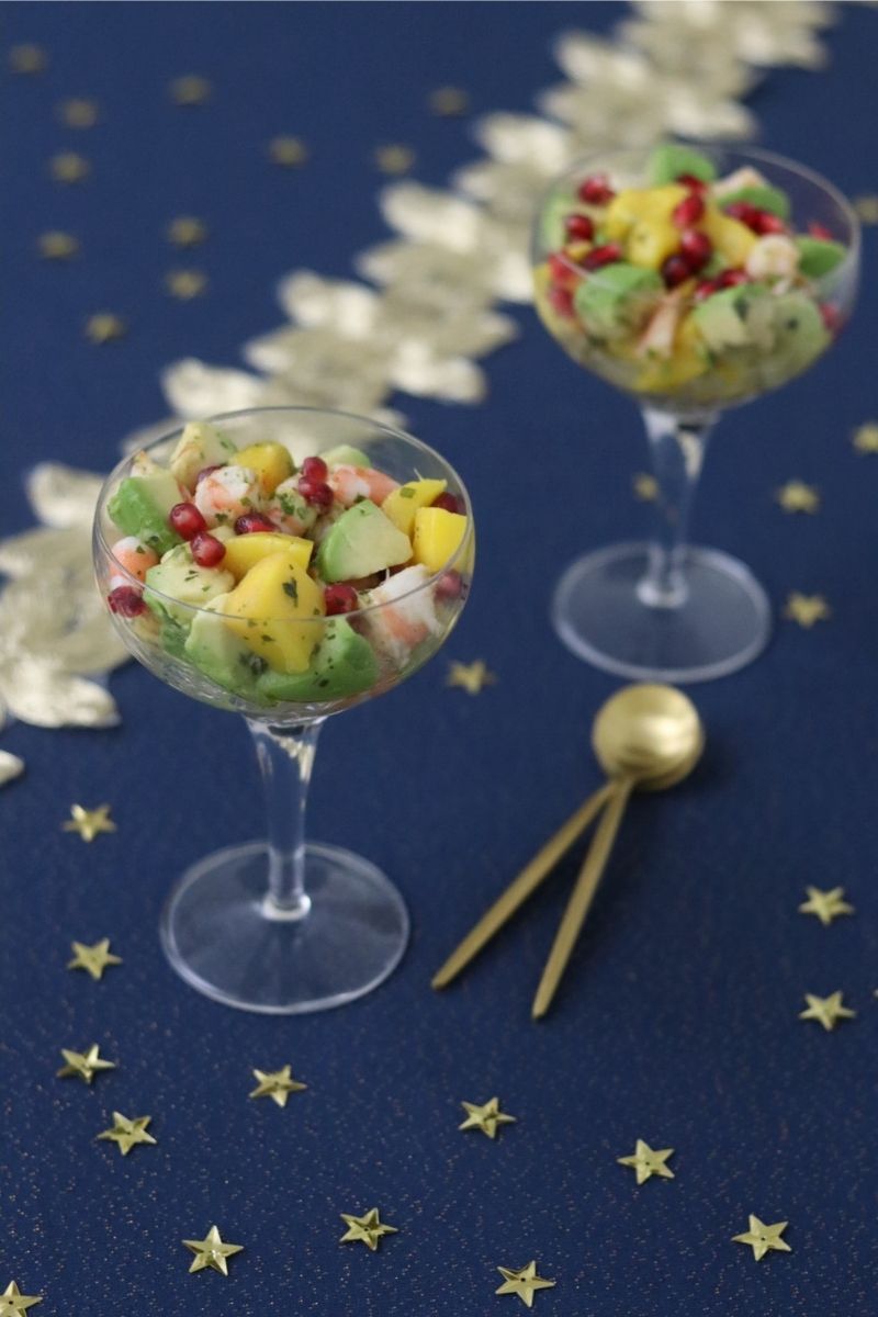 Mango avocado shrimp salad in 2 wine glasses on a night blue table cloth along with 2 golden spoons and gold stars to decorate