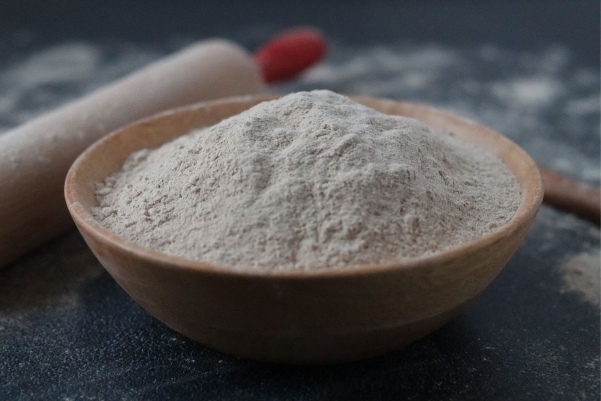 buckwheat flour in a wooden bowl, a rolling pin and a wooden spoon in the background