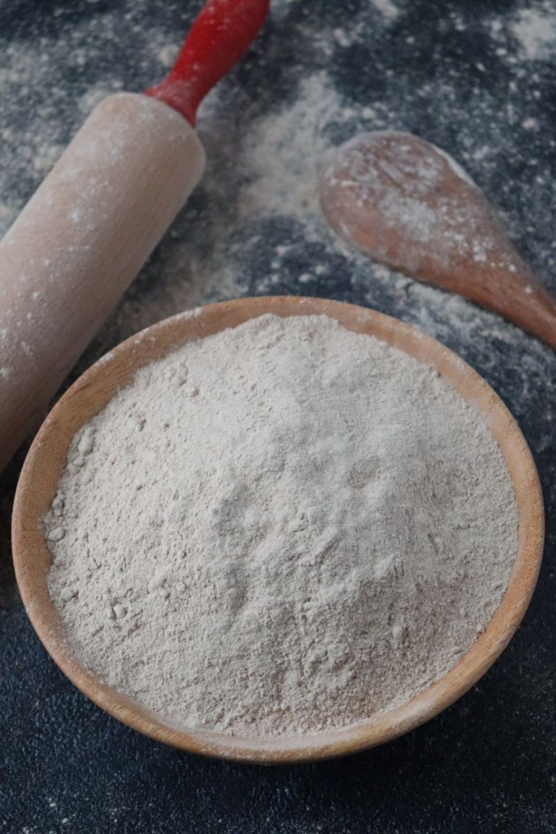 buckwheat flour in a wooden bowl, a rolling pin and a wooden spoon in the background